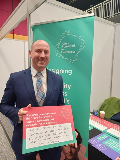 Neil Gray MSP smiles & holds up a hand written card in support of the Future Framework..
