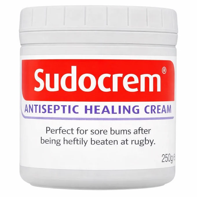 A Sudocrem container with red labeling reading "ANTISEPTIC HEALING CREAM." Text humorously suggests it’s for “sore bums after being heftily beaten at rugby.”