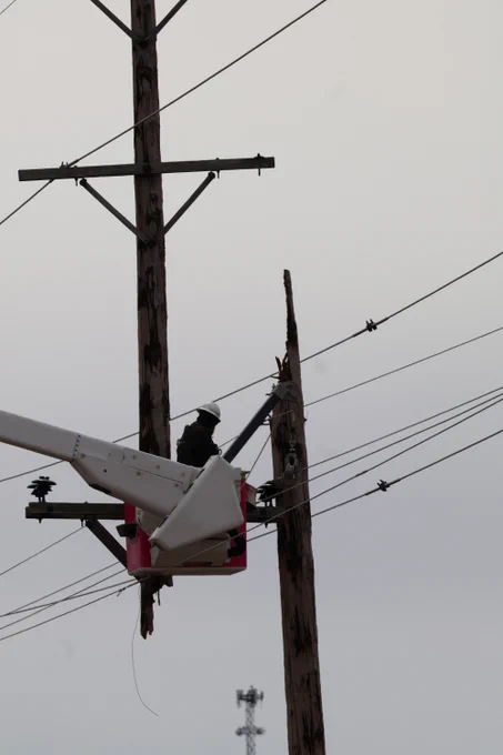 A line worker elevated in a bucket truck removing a broken utility pole so power can be restored. 