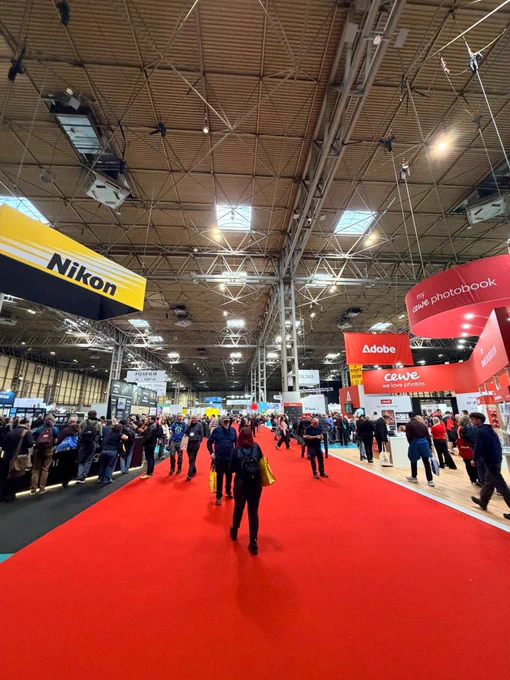 Image shows the entrance to the UK Photo Show 2026 with large boards advertising Adobe, Canon, and Nikon. 