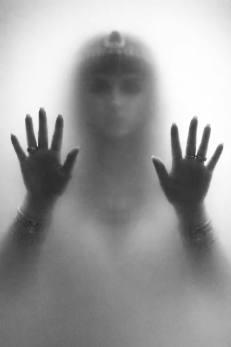 A human figure (Cleopatra) behind frosted glass with both hands pressed forward, fingers spread and sharply outlined against an otherwise indistinct silhouette.