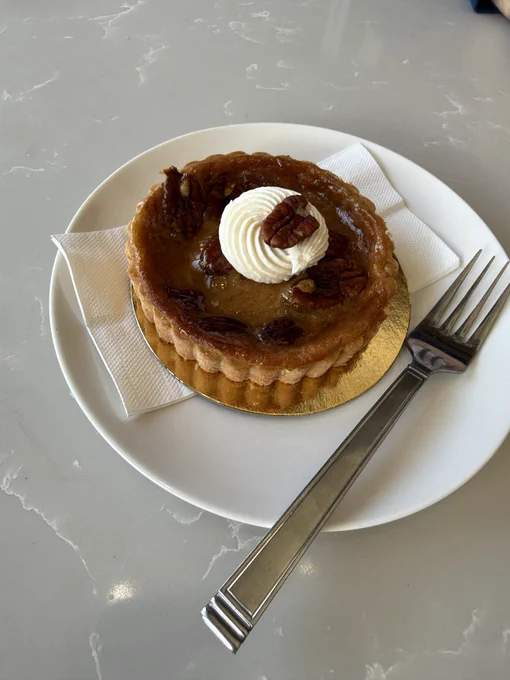 A small pecan pie on a white plate with a fork beside it.