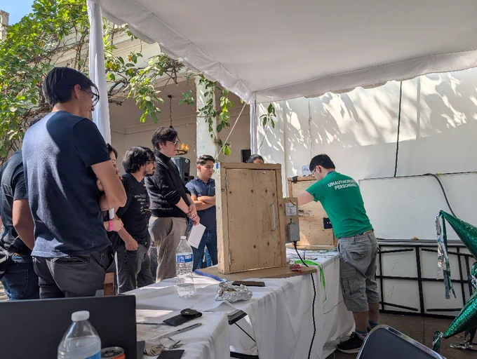several people surrounding a physical security village mini door being instructed by Terry, a staff member, in a green "unauthorized personnel" shirt