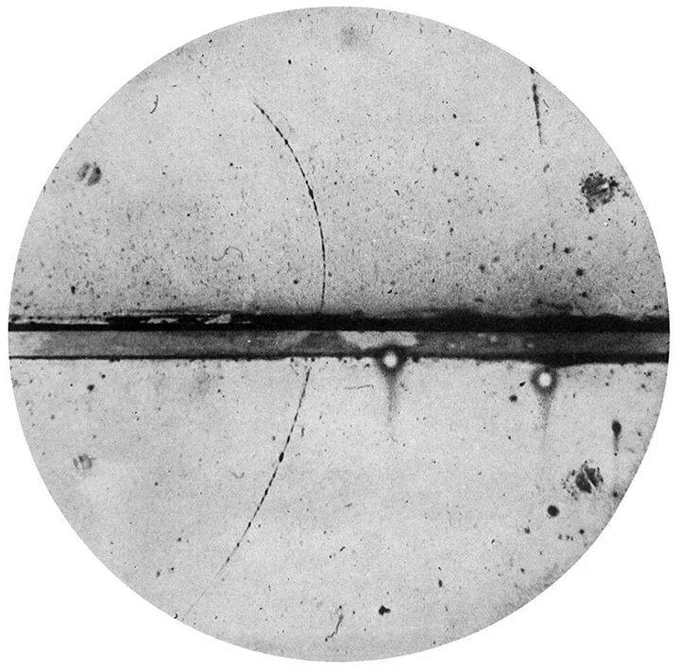Cloud chamber photograph by Anderson, the first positron ever observed. A 6 mm lead plate separates the upper and lower halves of the chamber. The deflection and direction of the particle's ion trail indicate the particle is a positron.