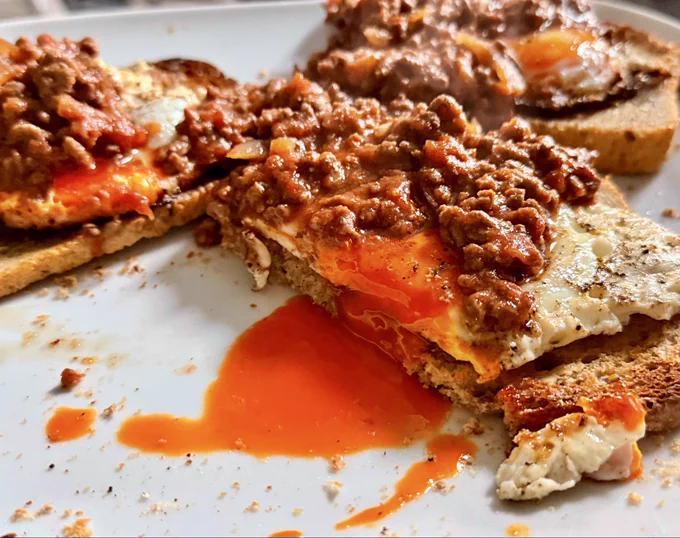 Fried eggs with deep orange yolk on homemade bread with bolognaise on top.