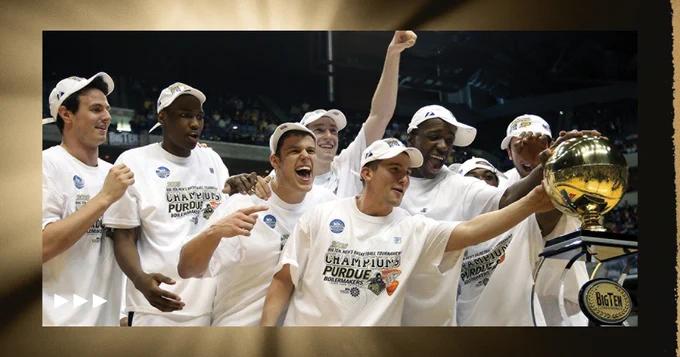 A group of smiling individuals wearing matching white T-shirts and caps celebrate winning a basketball championship. They are joyfully gathered around a shiny trophy with a "Big Ten" logo visible on a wall nearby.