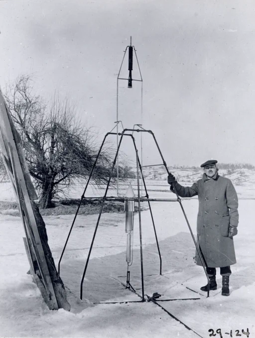 On a snowy March 16, 1926, Dr. Robert H. Goddard rests his hand on the testing frame supporting his liquid fuel rocket at Ward Farm in Auburn, Massachusetts. A wooden door is propped up at an angle next to the frame where Goddard\u2019s assistant, Henry Sachs, later sheltered after lighting the rocket. 