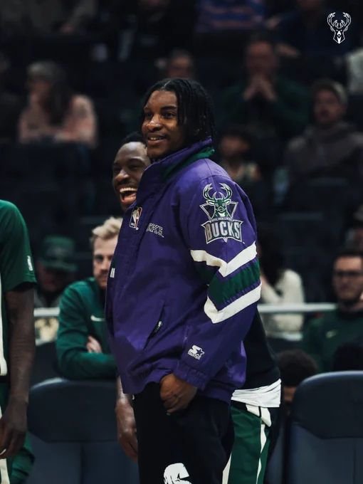 A photo of Kevin Porter Jr. smiling while wearing a retro purple Bucks jacket.