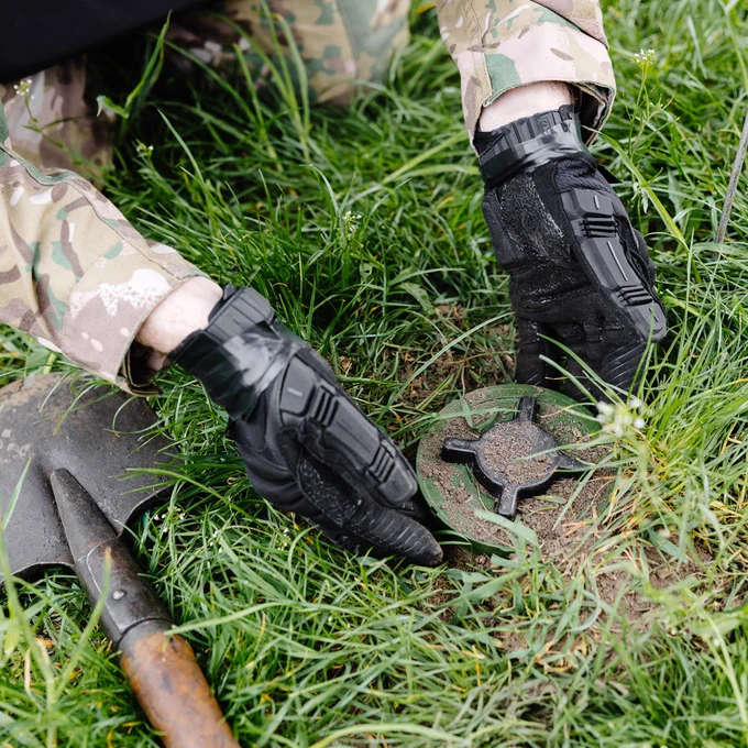 The arms of a person removing a landmine from the ground.