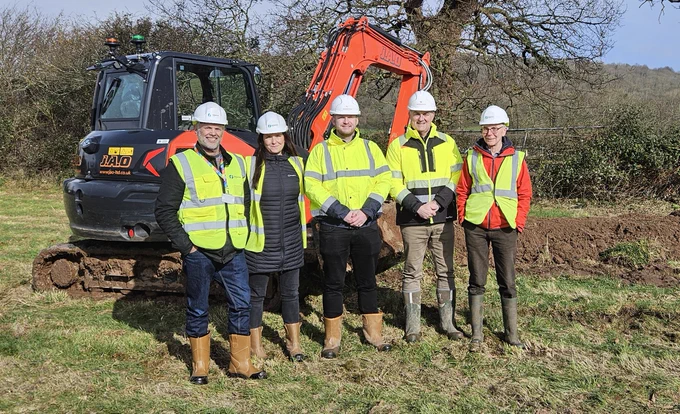 5 People standing in a field in front of a digger