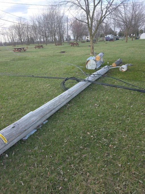 A transformer and utility pole with wires lay on the ground after wind knocked them over.