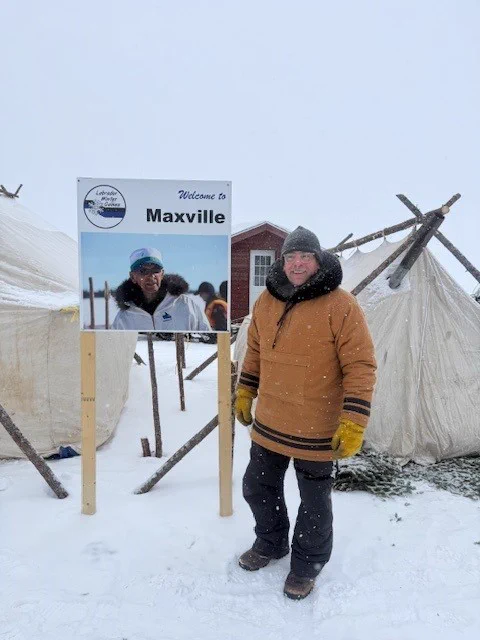 man in a brown parka and winter hat poses and smiles for the camera.