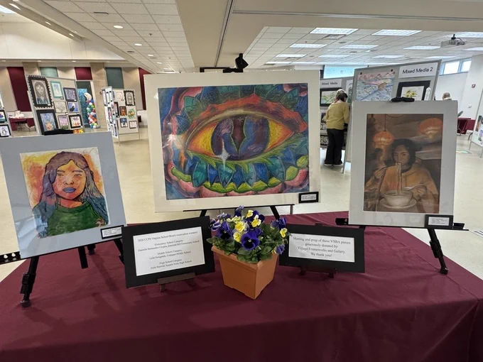 three matted pieces of artwork on display with flowers in a pot on the table in front of them and 2 signs