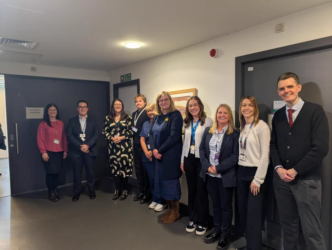 Public Health and Women's Health Minister Jenni Minto standing in a line with Siobhan Boyle of Thrive under 5, Dr Max Peluso, Dr Liz Bryden, Andrew Cushing of Glasgow City Health and Social Care Partnership, Marie McMenamin, Family Wellbeing Worker Hannah Stewart,
Kenna Campbell of Glasgow City Health and Social Care Partnership, Lianne Thomas from Glasgow Life, and Senior Community Link Worker Stuart Miller. The group is standing in a hallway at Peat Road Medical Practice in Glasgow, dressed in business and casual attire, posing for a photo indoors.