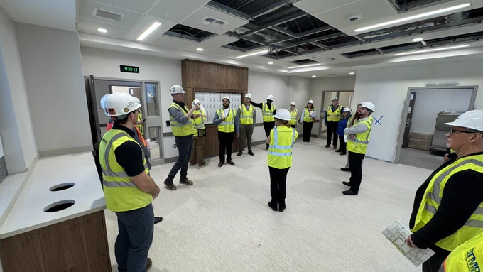 People wearing high visibility vests and hard hats tour construction site.