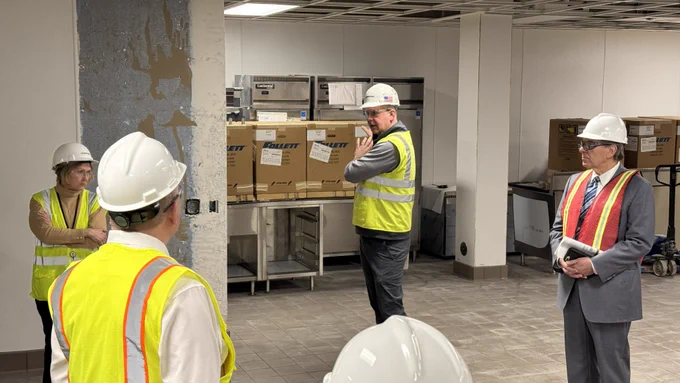 People wearing high visibility vests and hard hats tour construction site.