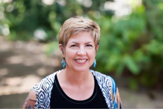 Headshot of Mary Brownell, Ph.D., smiling in a natural setting with greenery. 