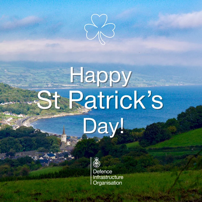 Scenic coastal village with green hills and blue sea under a partly cloudy sky, overlaid with 'Happy St Patrick’s Day!' text.