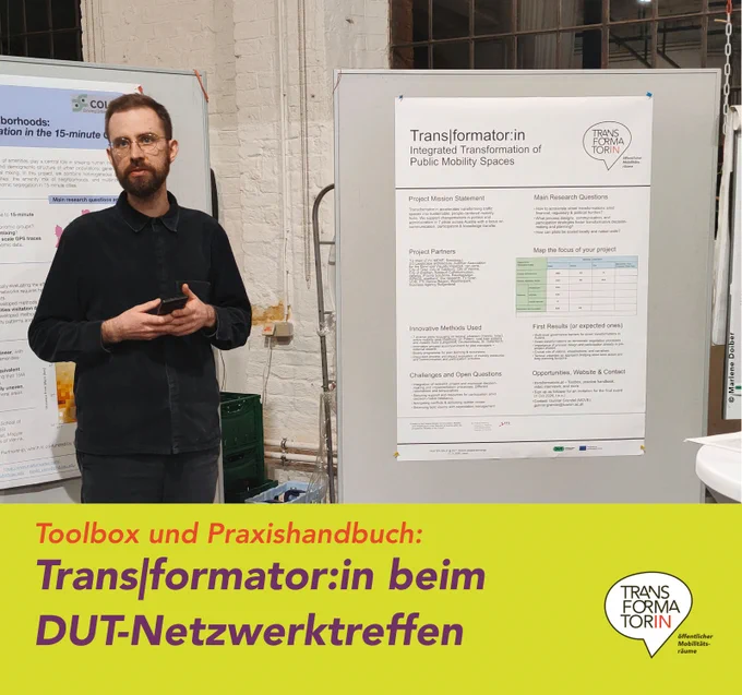 In einer alten Industriehalle (Ziegelmauer). Mann mit Vollbart trägt vor einer Posterwand der Trans|formator:in vor.
Überschrift: Transformator:in beim DUT-Netzwerktreffen
Subline: Toolbox und Praxishandbuch
Logo: Transformator:in, Logozusatz: öffentlicher Mobilitätsräume
