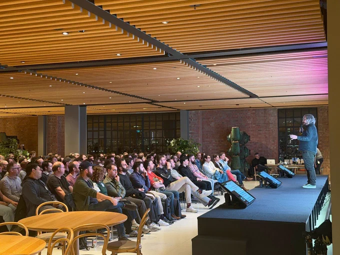 Darryl is on a stage in the Apple offices presenting to a large room of people watching him.