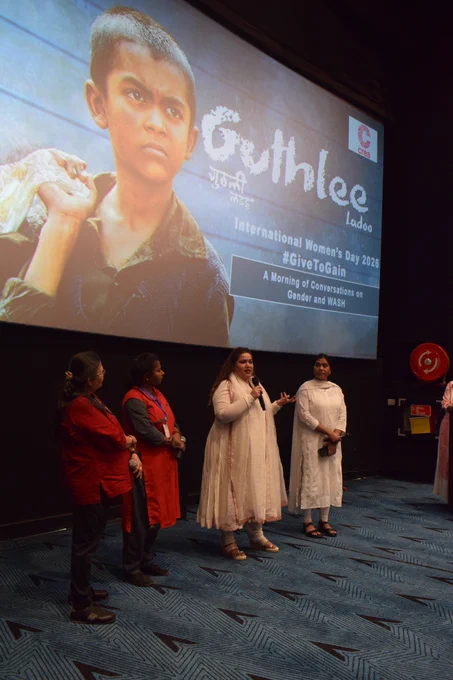A panel discussion in a cinema auditorium, where four women stand on stage speaking into microphones beneath a large screen displaying the “Guthlee Ladoo” film poster.
