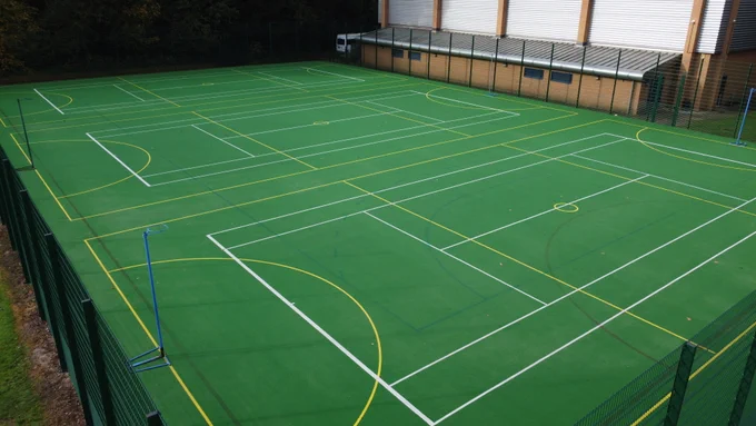 Close up shot of MUGA with white and yellow markings, and basketball and netball hoops in 6 different areas