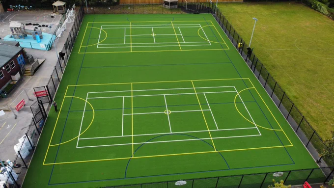 Aerial view of a fenced multi-sport court with markings for  football, tennis, and basketball on a green surface.