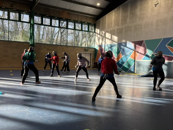 Several people are fencing in a sports hall.