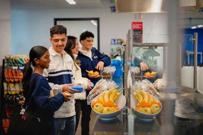 Students wait in line for food in a cafeteria.
