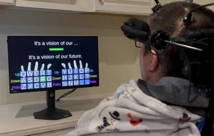 A person in a wheelchair with head gear on, looking at a computer screen