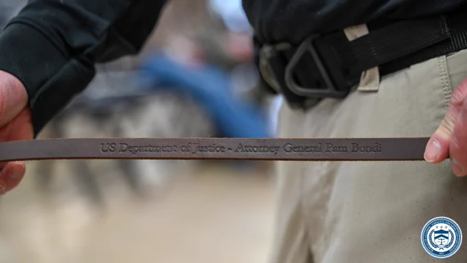 Close-up of a person holding a leather leash engraved with 'US Department of Justice - Attorney General Pam Bondi'.