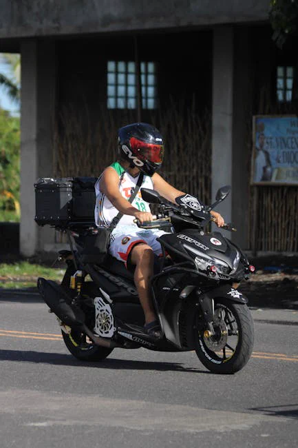 Adult motorcyclist riding a black scooter on a sunny urban road.