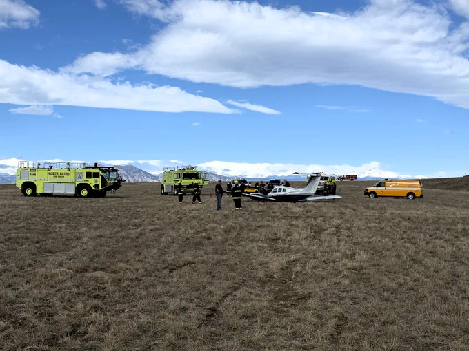 Image of an airplane in a dry grassy field surrounded by emergency vehicles 