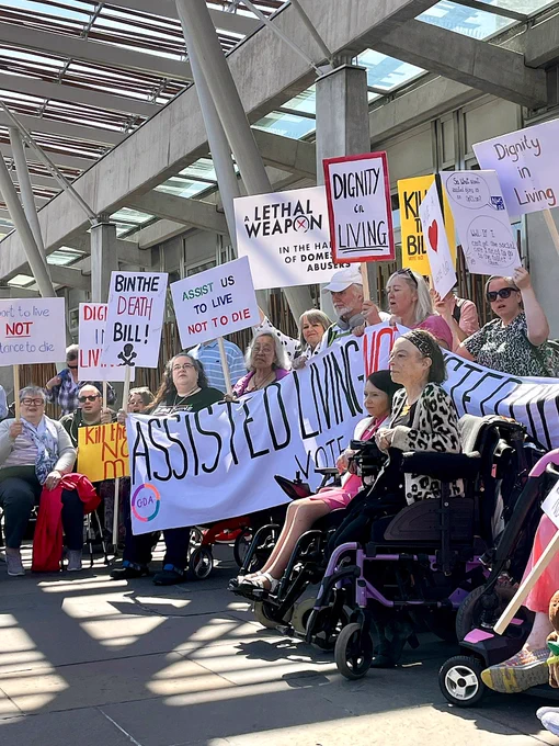 Demonstration last May outside the Scottish Parliament with many disabled people holding placards saying assist us to live not to die, dignity in living,  bin the death Bill.