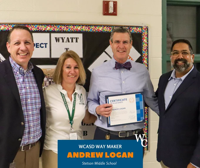 Andrew Logan holding a certificate of achievement at Stetson Middle School, standing with three adults in front of a bulletin board.