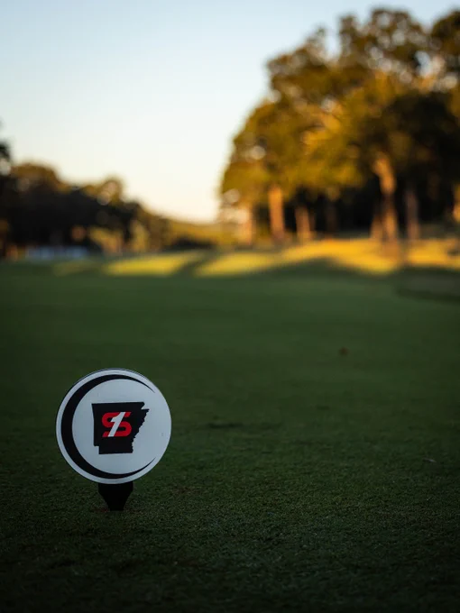 Golf course landscape during sunset, featuring a Bridgestone tee marker. Trees line the background.