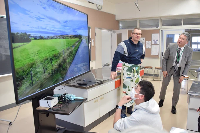 Three people stand in front of a monitor looking at a Google Street View screenshot, trying to work out where it is.