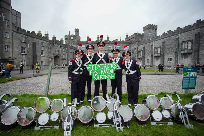 Members of The Ohio State University Marching Band holding a “St Patrick’s Festival Kilkenny” sign  in front of Kilkenny Castle.