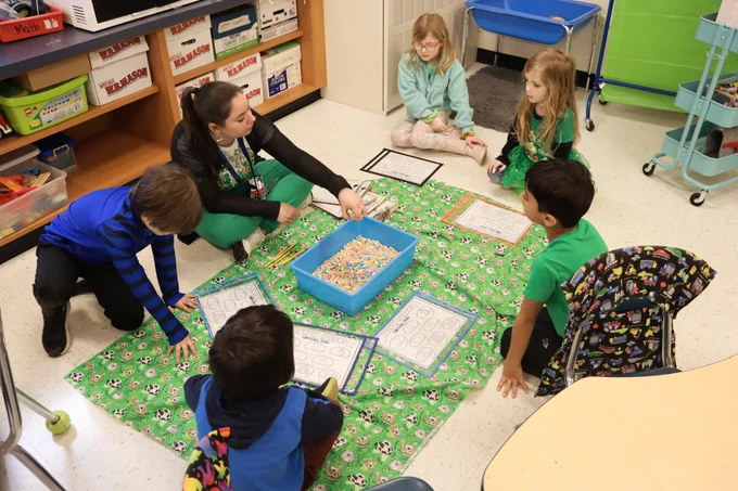 students and teacher sitting on a green sheet ready to do a st. pattys day activity