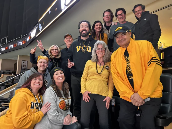 A group of people in stadium stands looking at the camera, all wearing V-C-U gear or black and gold.