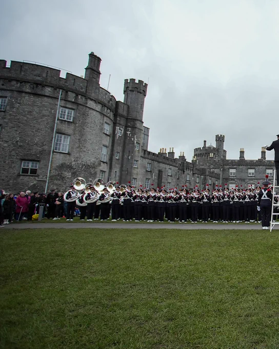 The Ohio State University Marching Band performing in front of a castle in Ireland. The weather is overcast.