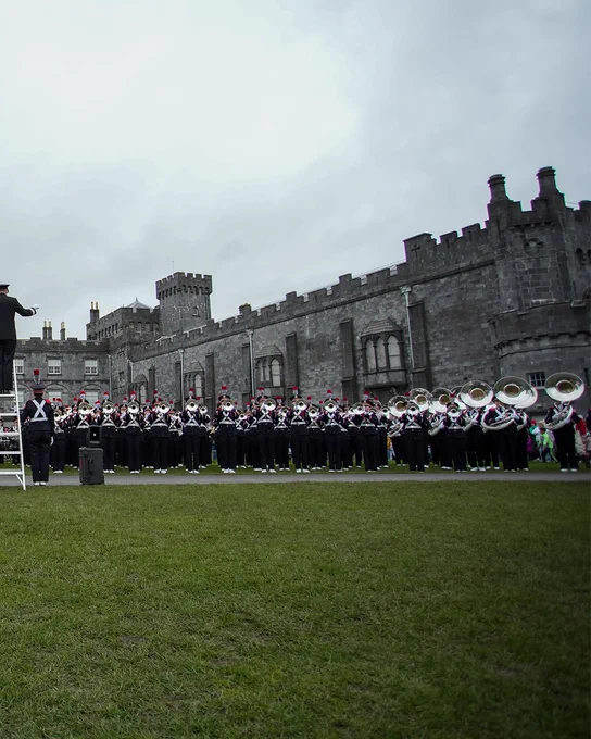 The Ohio State University Marching Band performing in front of a castle in Ireland. The weather is overcast.