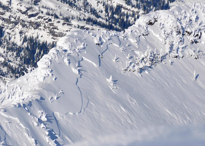Snowy alpine ridge with scattered snow-laden trees.