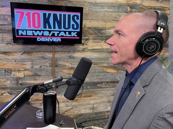 SAC David Olesky with headphones on during live radio interview. Station sign on screen in background