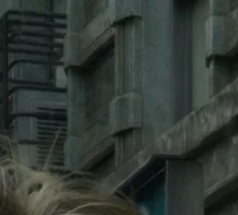 A demo screenshot from Resident Evil Requiem with "DLSS 5 ON", showing the building behind Grace. The texture has been smoothed out and has lost definition. The texture is smoothed more like marble, and the brickwork is barely legible. Interestingly, this is one case where contrast appears lower than the original.