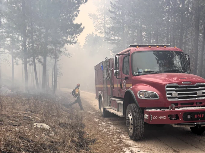 Image of a red fire engine on a dirt road in a forest with frost on the ground and smoke rising from the trees