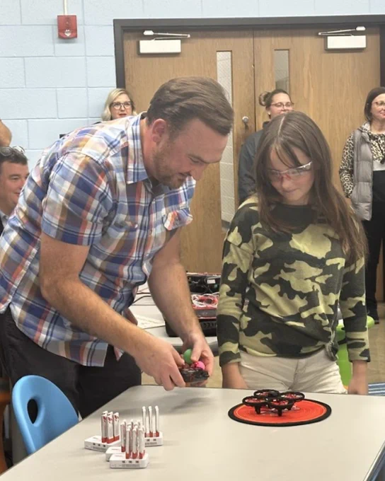 Teacher helping young student with classroom drone. 