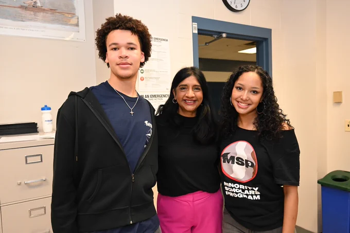 Lt. Gov. Aruna Miller (Middle) and two students standing together in a classroom, one wearing a Minority Scholars Program t-shirt, smiling and posing for a photo.
