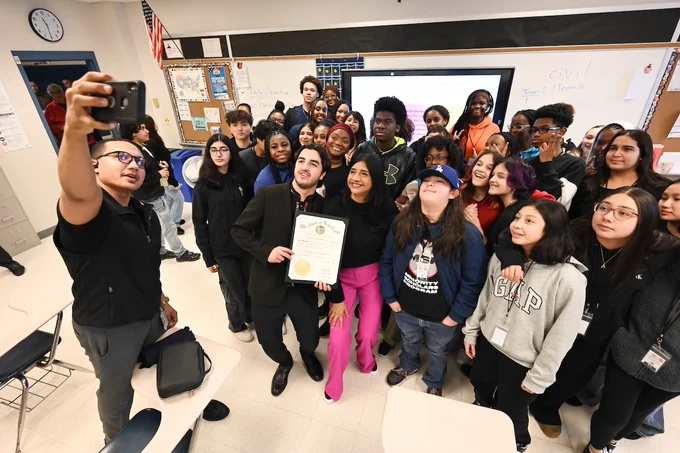 A group of students and Lt. Gov. Aruna Miller(Middle) gather in a classroom for a group selfie, with one person holding a certificate. 