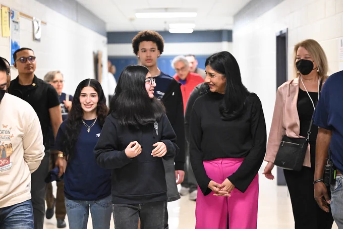 Students and Lt. Gov. Aruna Miller walking through a brightly lit school hallway engaged in conversation and activity.